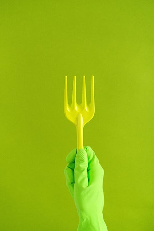 Free Crop anonymous person in rubber glove showing plastic garden rake against green background Stock Photo