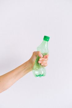 白色背景下，一只成年人的手正在挤压一个空的绿色塑料瓶，以促进回收