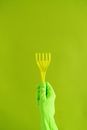 Crop anonymous person in protective gloves demonstrating plastic supply for household needs on green background