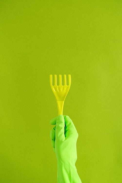 Free Crop anonymous person in protective gloves demonstrating plastic supply for household needs on green background Stock Photo