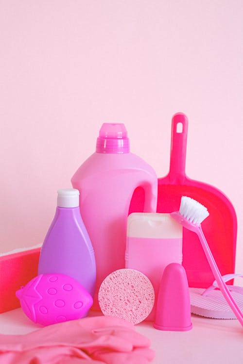 Set of assorted plastic containers with gloves brush and scoop for cleaning routine on pink background