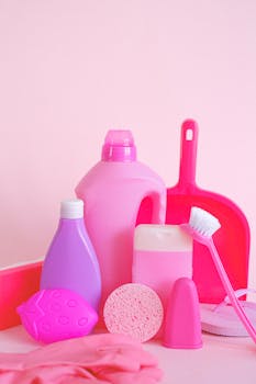 Set of assorted plastic containers with gloves brush and scoop for cleaning routine on pink background