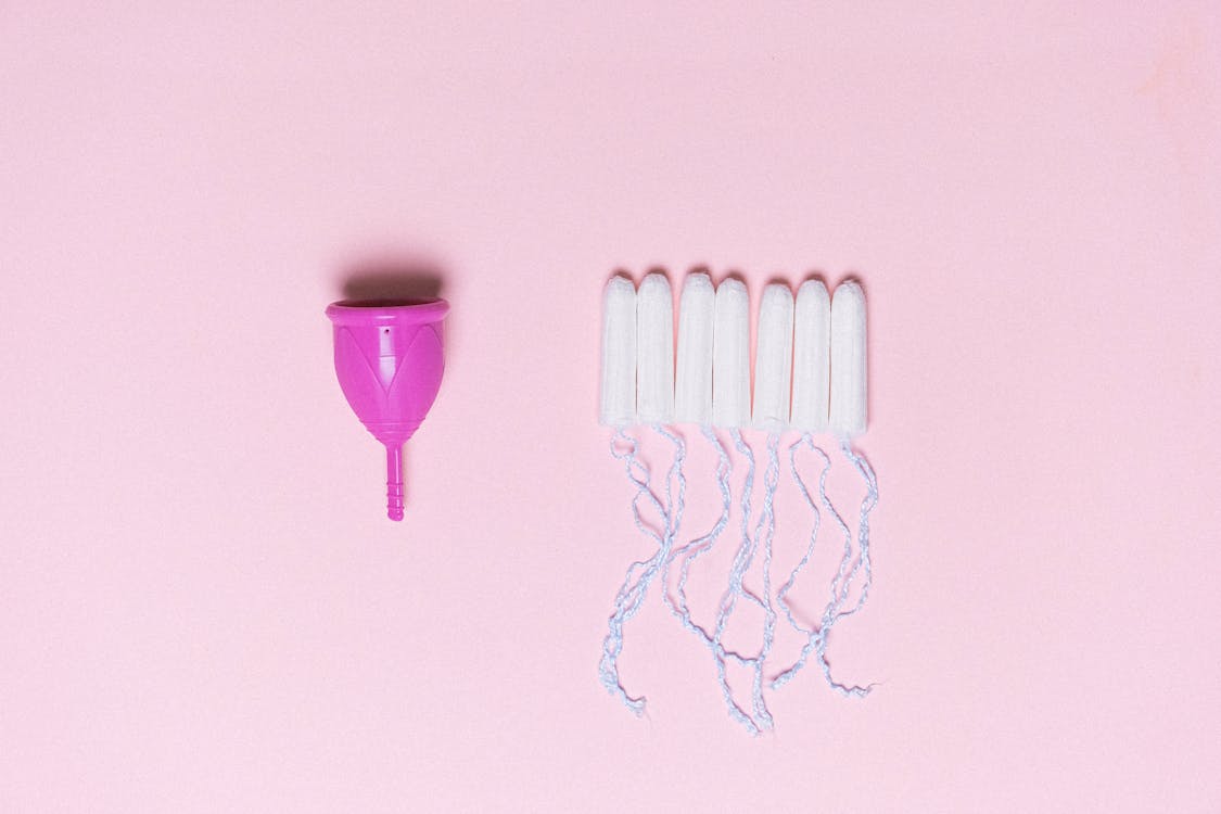 Menstrual cup and tampons arranged on pink surface