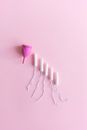 Top view arrangement of pink menstrual cup placed on light pink surface near tampons