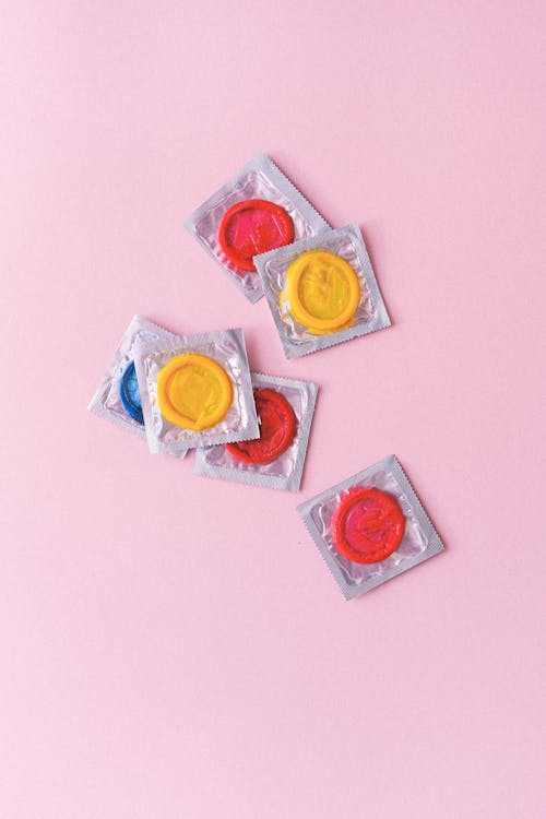 Multicolored condoms heaped on pink background