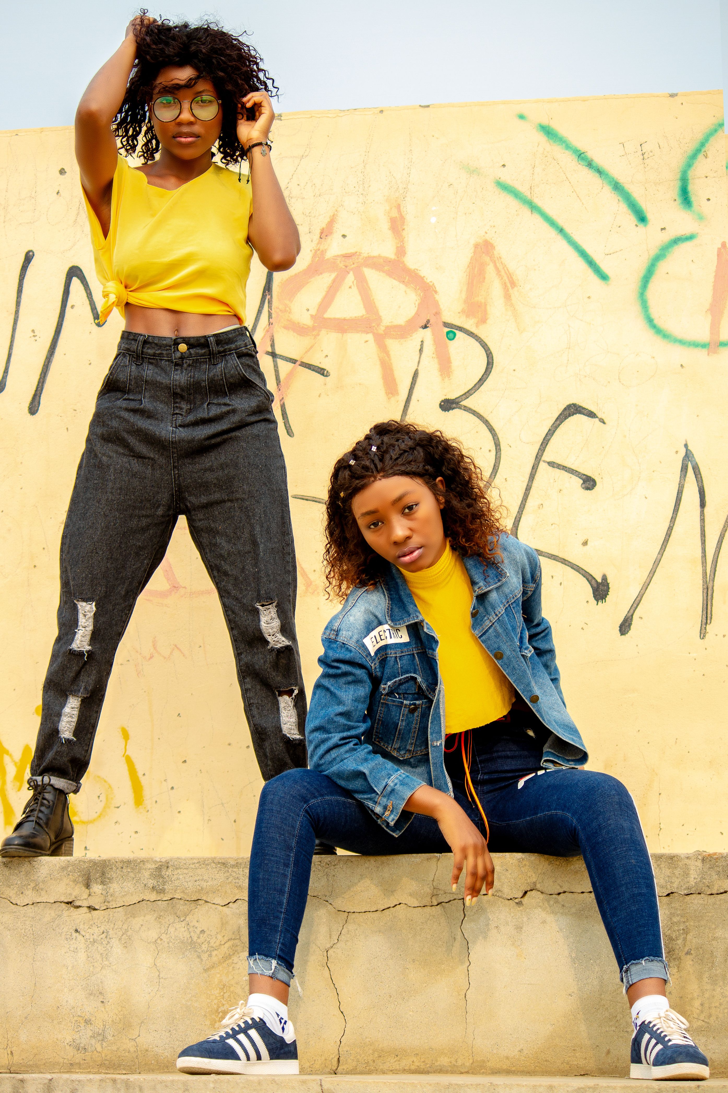 Duas jovens confiantes posam em trajes modernos diante de uma parede coberta de grafite.