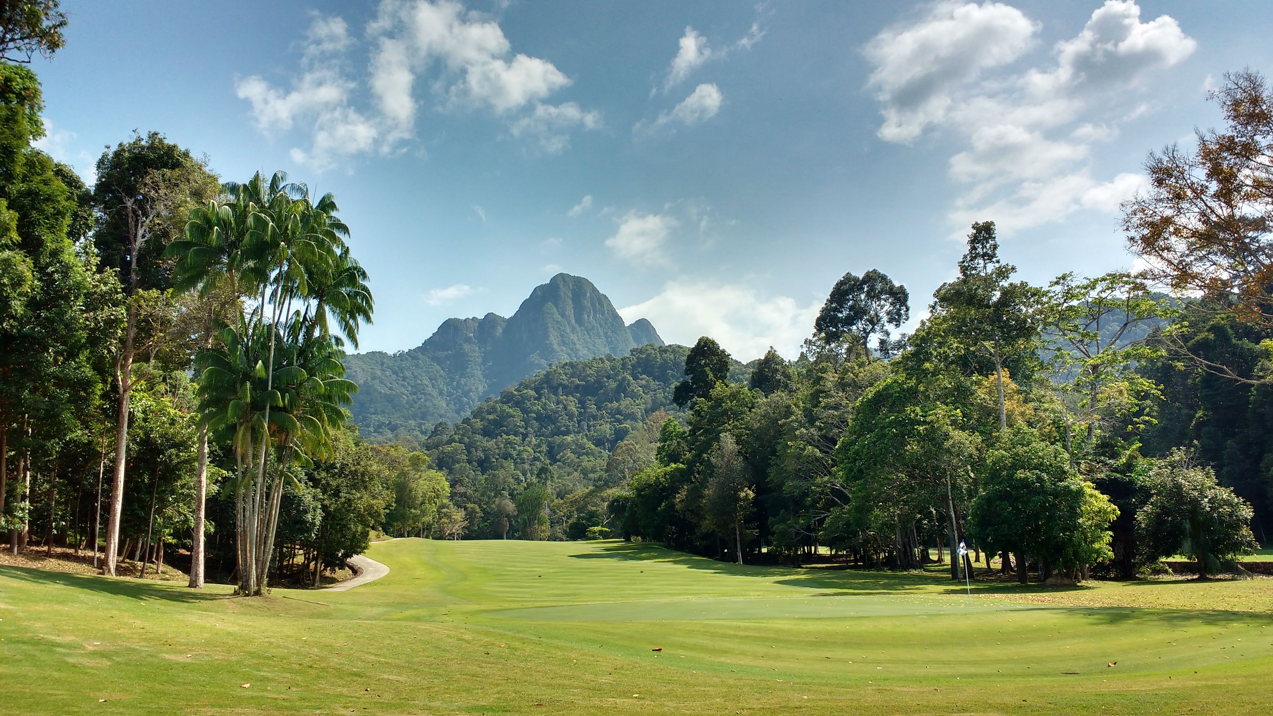 Golfers on a manicured fairway framed by tropical hills at sunrise