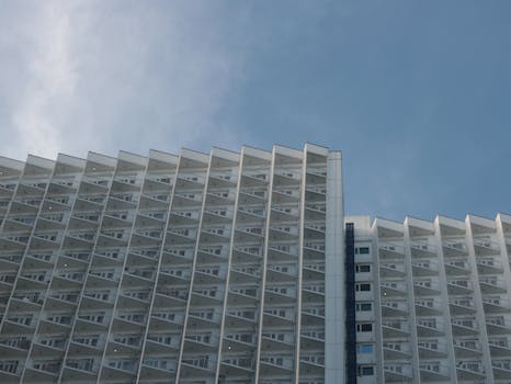 Tall modern residential building with numerous balconies set against a bright blue sky.