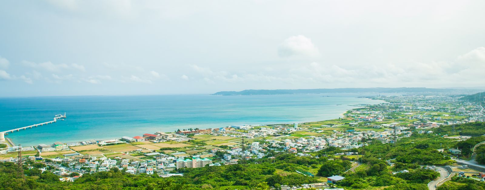 Calm turquoise water of ocean washing shore with small town and green tropical forest under cloudy sky