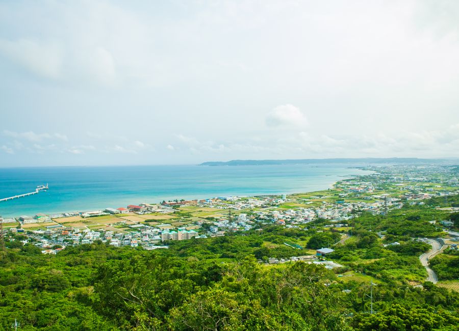 Calm turquoise water of ocean washing shore with small town and green tropical forest under cloudy sky