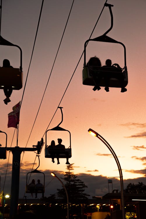 From below of unrecognizable traveler silhouettes in cabins on ropeway under cloudy sky at sunset