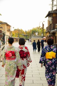 一位身着传统服饰、佩戴装饰品的匿名少数族裔女性，正漫步于城市房屋间的街道上，背影渐行渐远