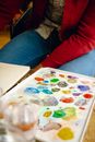 Crop anonymous painter sitting at table with bright paint palette near canvas while working on project