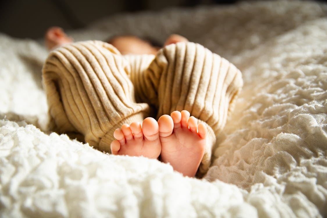 日光の下で柔らかいベッドで寝ている匿名の裸足の赤ちゃん