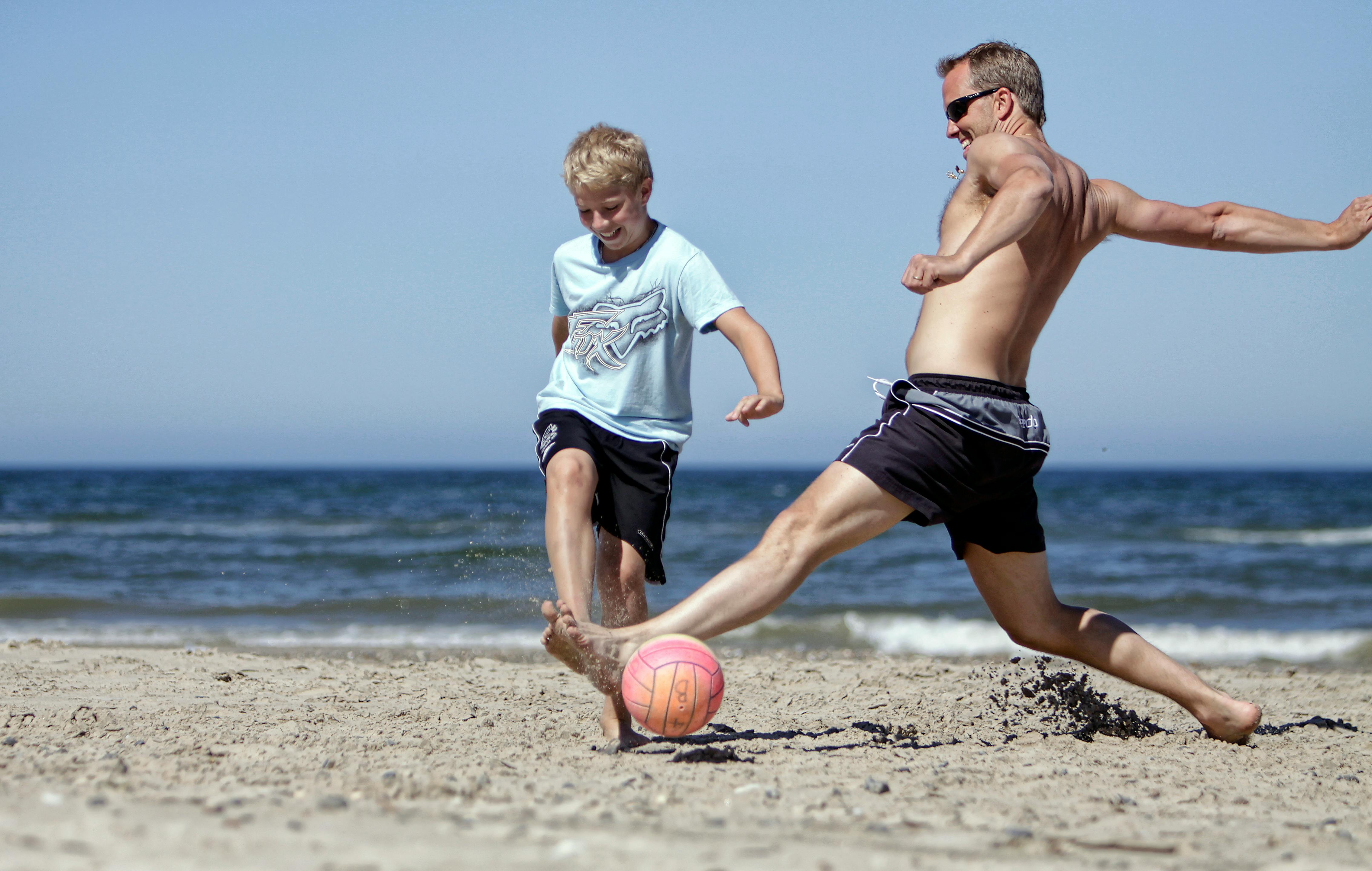 man and boy playing soccer on beach