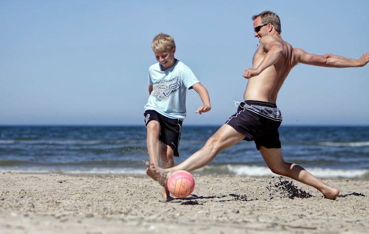 Man And Boy Playing Soccer On Beach