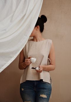 女人在窗帘后的轻松时尚氛围中享用咖啡