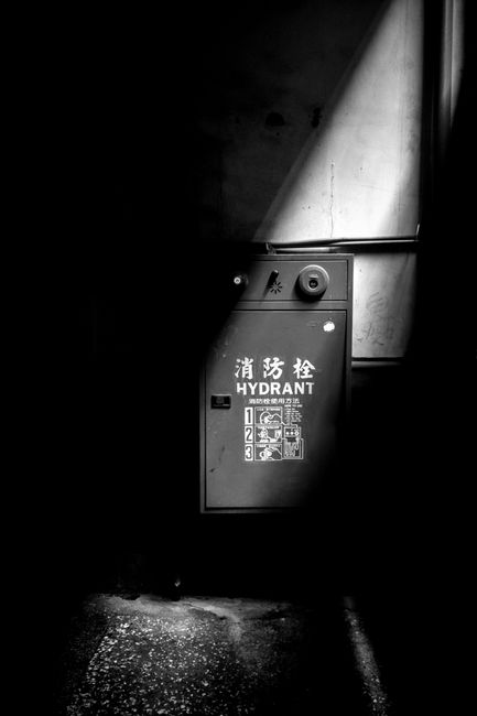 A black and white image of a fire hydrant cabinet in a dark, shadowy setting.