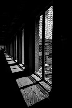 Black and white photo of corridor with intense chain link shadows on the floor.