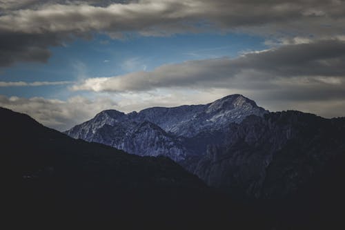 Spectacular landscape of massive rocky mountains with snowy peaks under cloudy blue sky at sundown