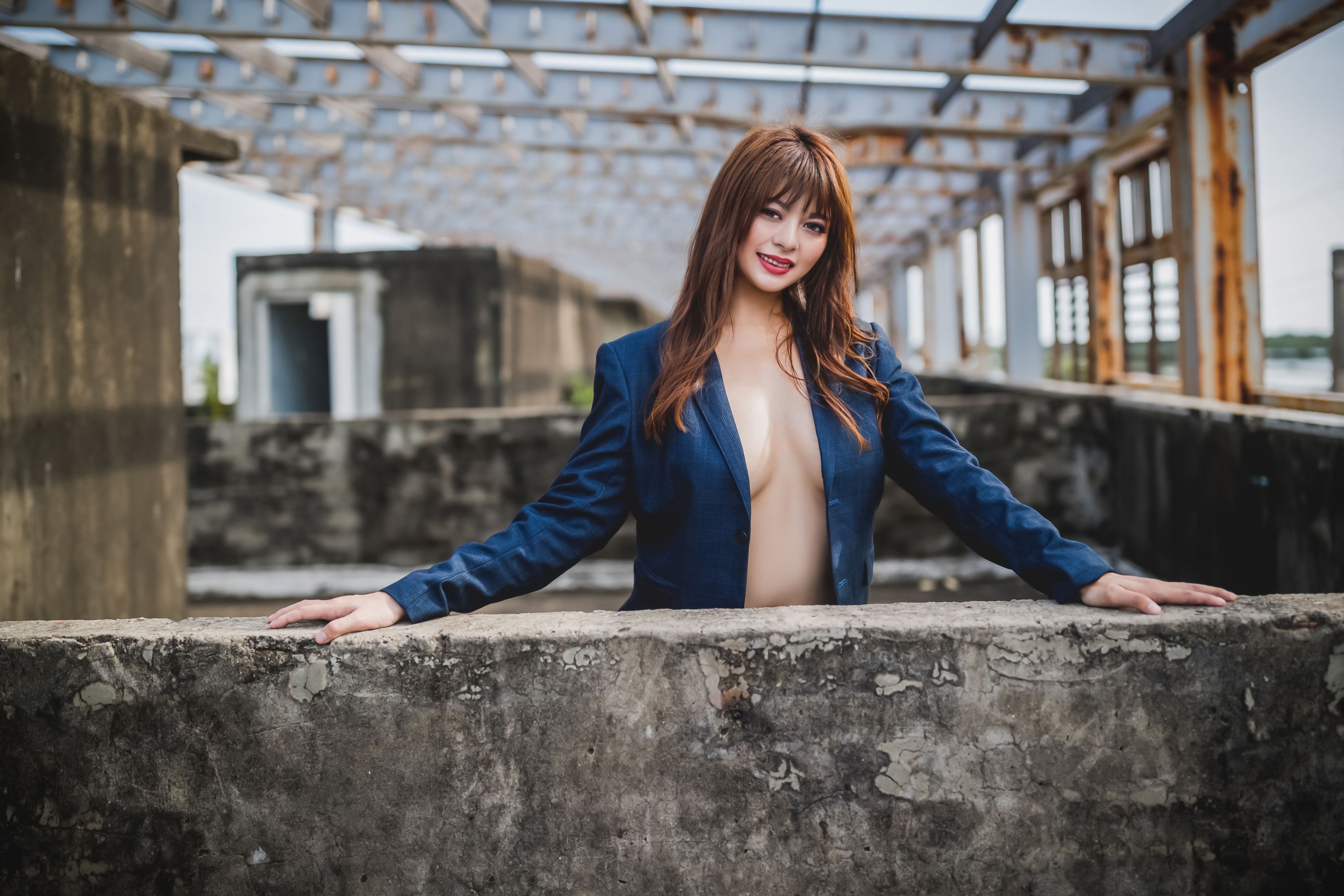 青いジャケットを着た自信に満ちた女性が、廃工場でポーズをとり、現代ファッションを披露しています。
