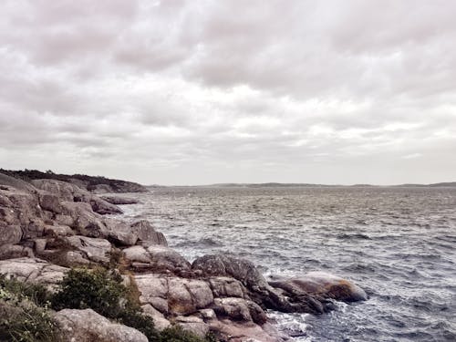 Brown Rock Formation Beside Body of Water Under Cloudy Sky