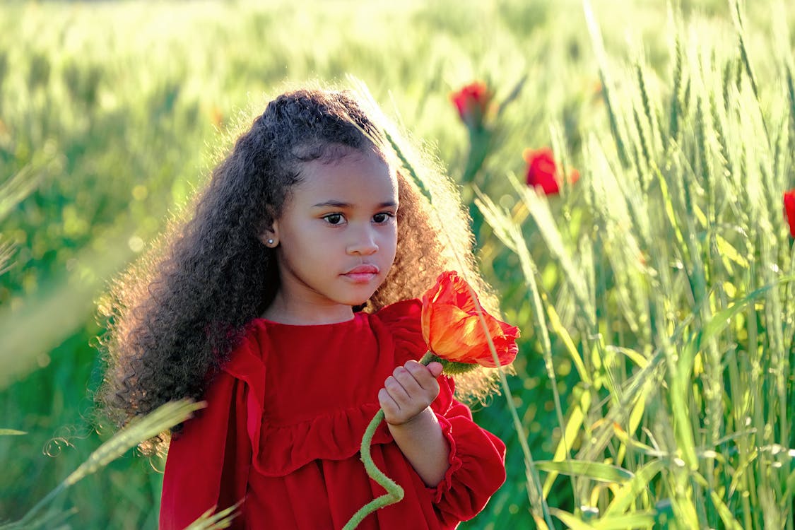 Charming black girl with red flower in abundant grassland