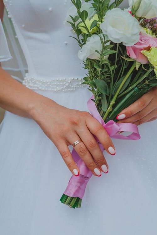 Free Crop woman in white wedding dress and ring holding bouquet of fresh flowers at daylight Stock Photo