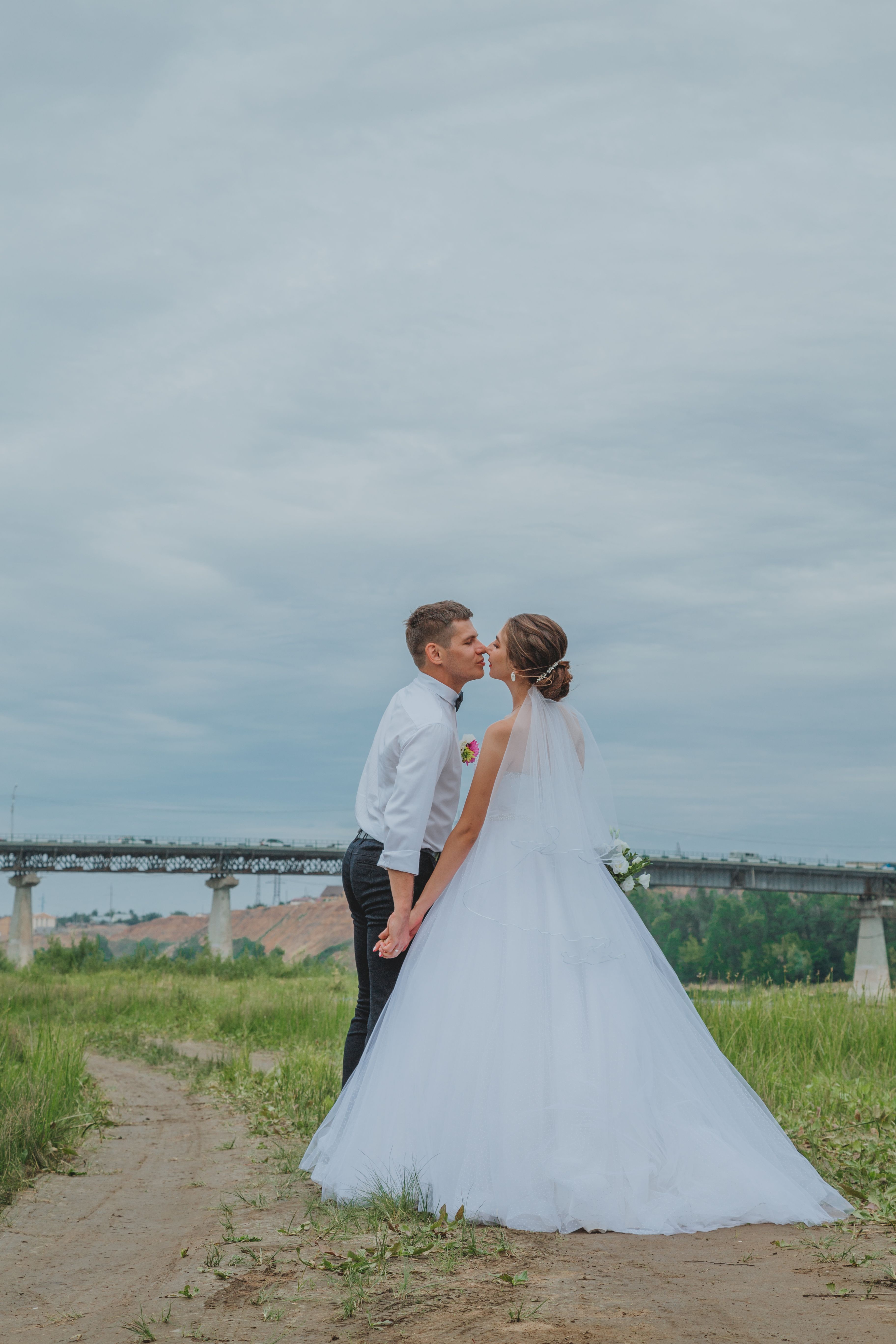一对身着优雅服装的新婚夫妇，在光天化日之下站在人行道旁接吻的侧影