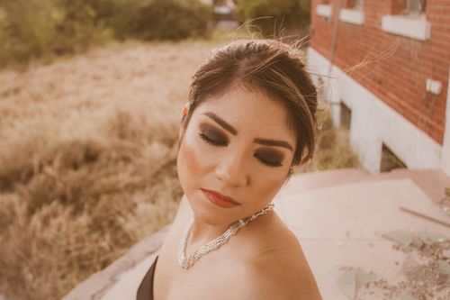 Free From above of charming female with bright eyeshadow standing with closed eyes on doorstep of brick house with pieces of glass near grassy field Stock Photo