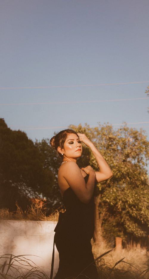 Free A woman in a black dress poses elegantly outdoors during sunset, exuding glamour and sophistication. Stock Photo