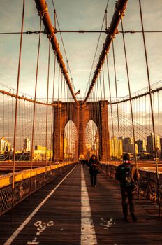 A scenic view of New York's Brooklyn Bridge at sunrise with pedestrians walking on the pathway.