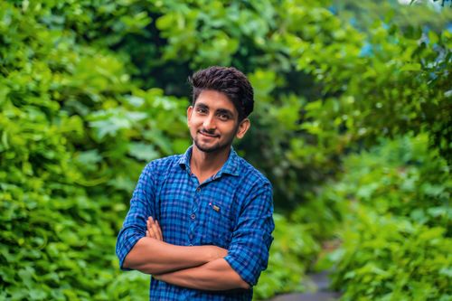 Free Young man in a checkered shirt with arms crossed, smiling against a lush green background. Stock Photo