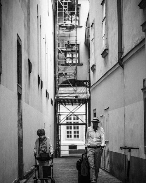 Free Grayscale Photo of an Elderly Woman and a Man Walking on an Alley Stock Photo
