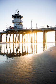 Huntington Beach Pier during sunset with reflections on wet sand.