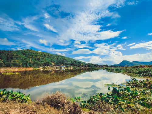 Free Serene pond reflecting blue sky and lush hills in scenic Assam, India. Stock Photo