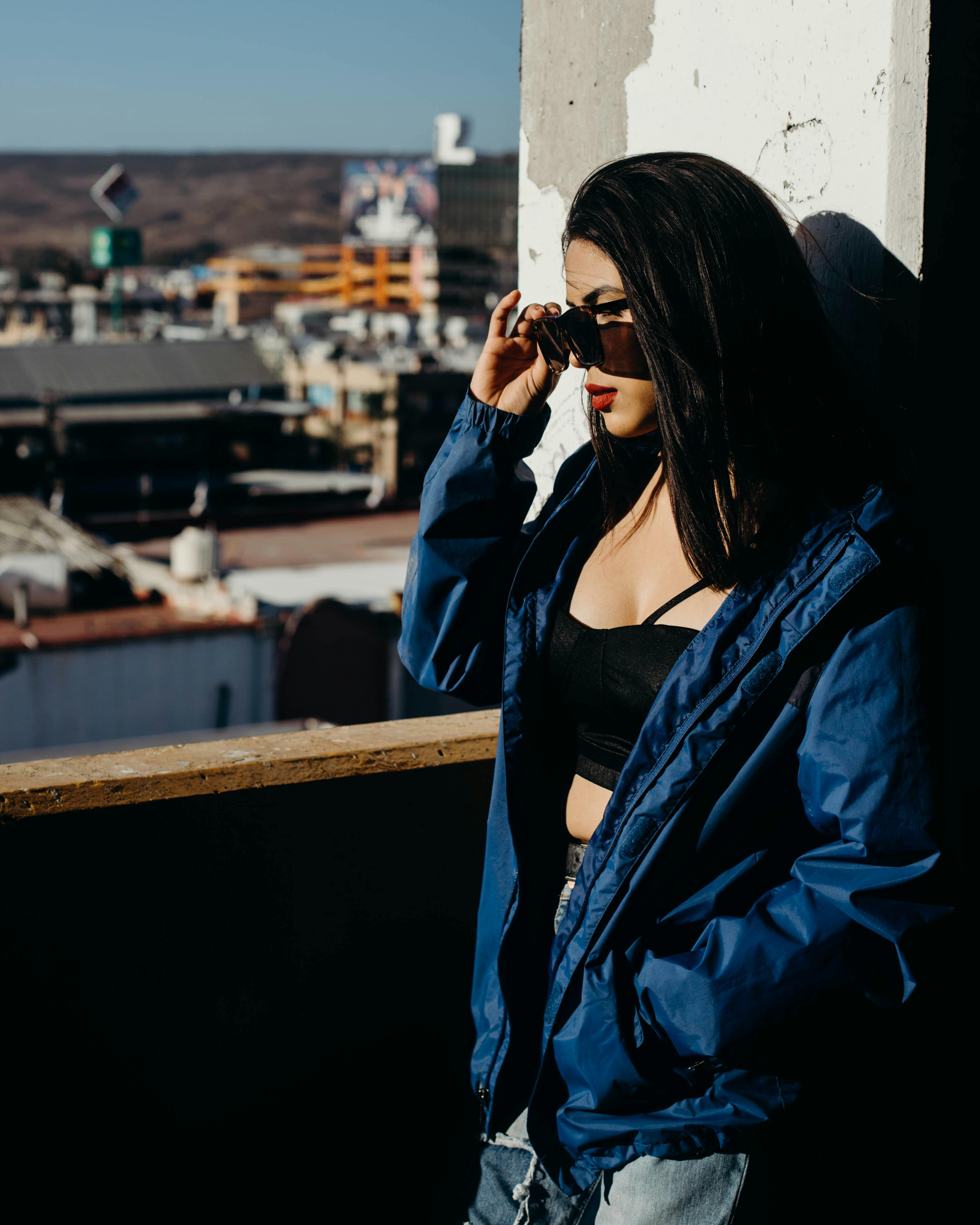 阳光明媚的日子里，一位戴着太阳镜、身穿蓝色夹克的时尚女性正在欣赏城市天际线