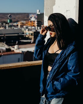 阳光明媚的日子里，一位戴着太阳镜、身穿蓝色夹克的时尚女性正在欣赏城市天际线