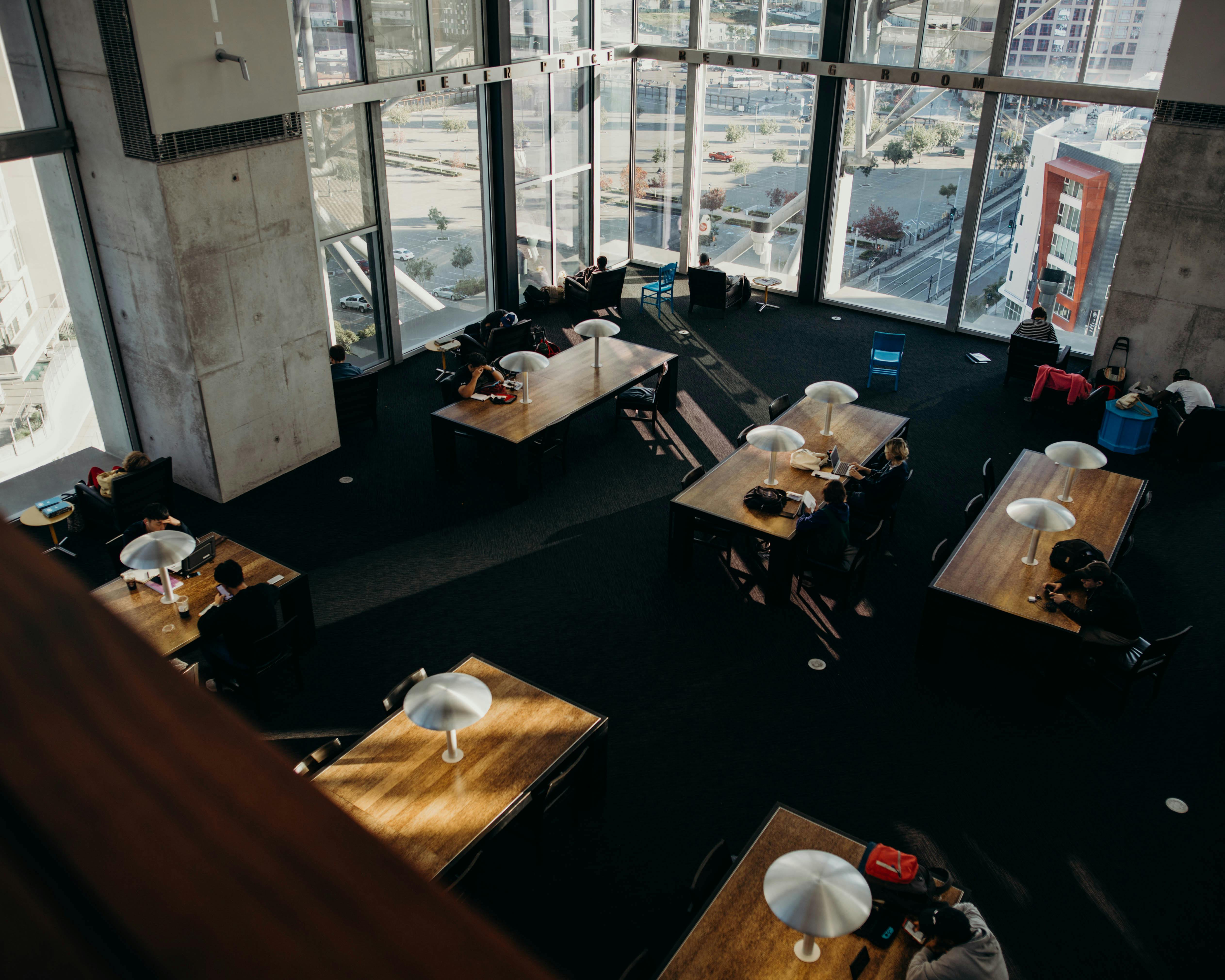 Bird's-eye view of a modern library with tables and people studying by large windows in San Diego, CA.