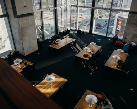 Bird's-eye view of a modern library with tables and people studying by large windows in San Diego, CA.
