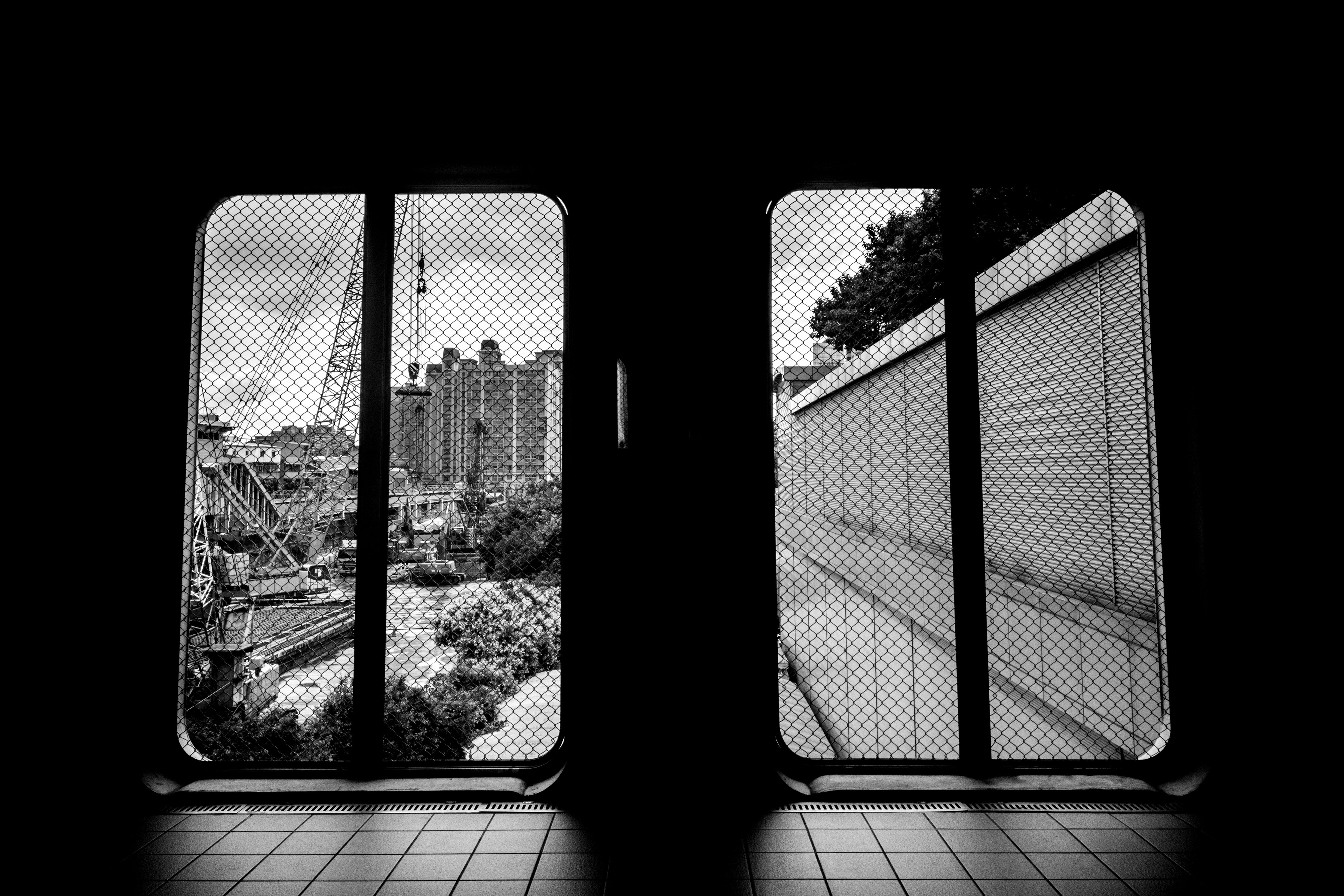 A striking black and white view of urban architecture through a mesh-covered window, showcasing city life.