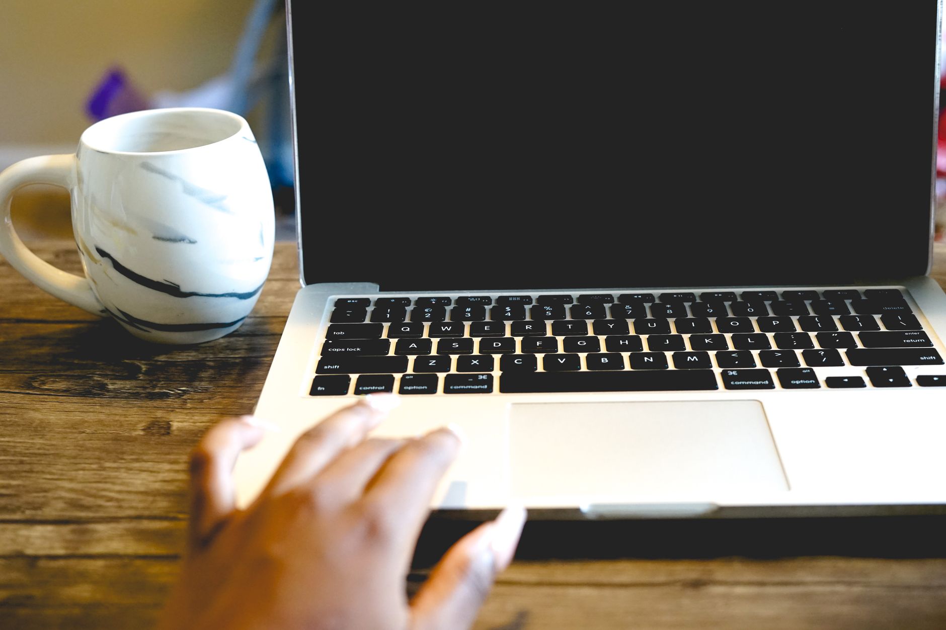 A close view of a hand on a laptop beside a marble mug on a wooden desk, ideal for remote work themes.