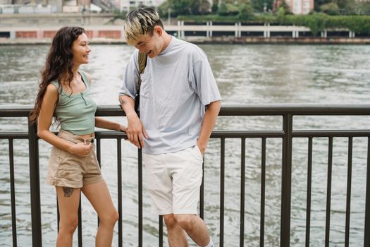 白天，一对微笑的多种族夫妇站在城市河边的长廊围栏附近