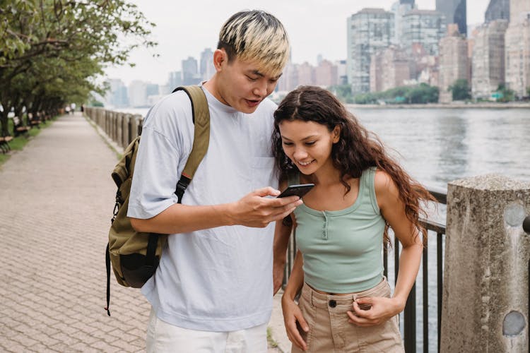 Content Young Multiracial Couple Using Smartphone On River Bank