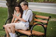 一对年轻夫妇共用一部智能手机，在公园长凳上享受户外休闲时光