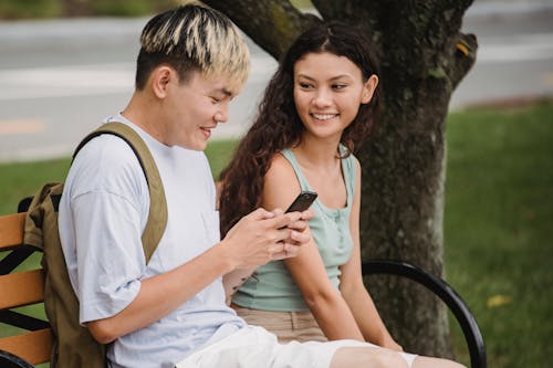 Çok ırklı çift Gülümseyen Akıllı Telefon Tarama Ve Parkta Iletişim