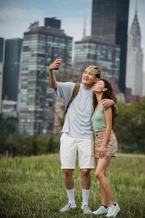 Full body of positive young diverse couple in stylish clothes hugging and taking selfie on mobile phone while spending holidays in New York City