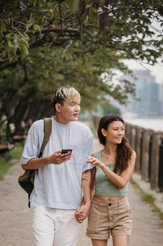一对亚洲夫妇手牵着手，幸福地沿着河边的海滨长廊散步，在户外享受着无忧无虑的一天