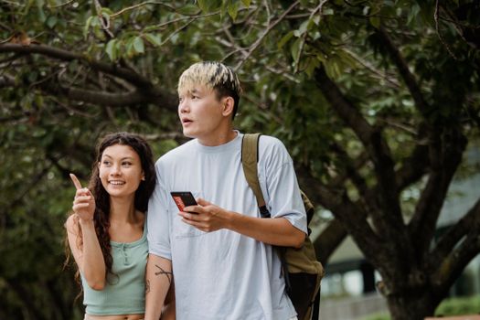 一对年轻夫妇手持智能手机，在绿树成荫的户外愉快地探索活动