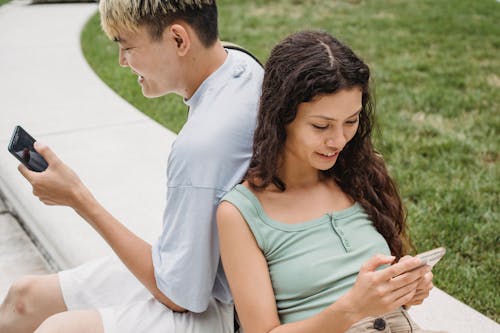 Free Crop diverse couple chatting on smartphones on street bench Stock Photo